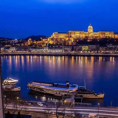 Intercontinental Budapest By Ihg Esterno foto The image shows a beautiful nighttime view of the Danube River in Budapest, Hungary. The river reflects the lights from buildings along the shore, creating a serene and picturesque atmosphere. In the background, the illuminated Buda Castle stands pro