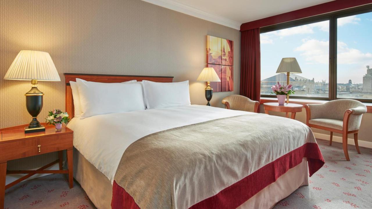 Intercontinental Budapest By Ihg Esterno foto The photo depicts a hotel room with a cozy and inviting atmosphere. There is a large bed with crisp, white linens, complemented by a decorative bedspread in a subtle color. On either side of the bed, there are bedside lamps providing soft lighting. 
