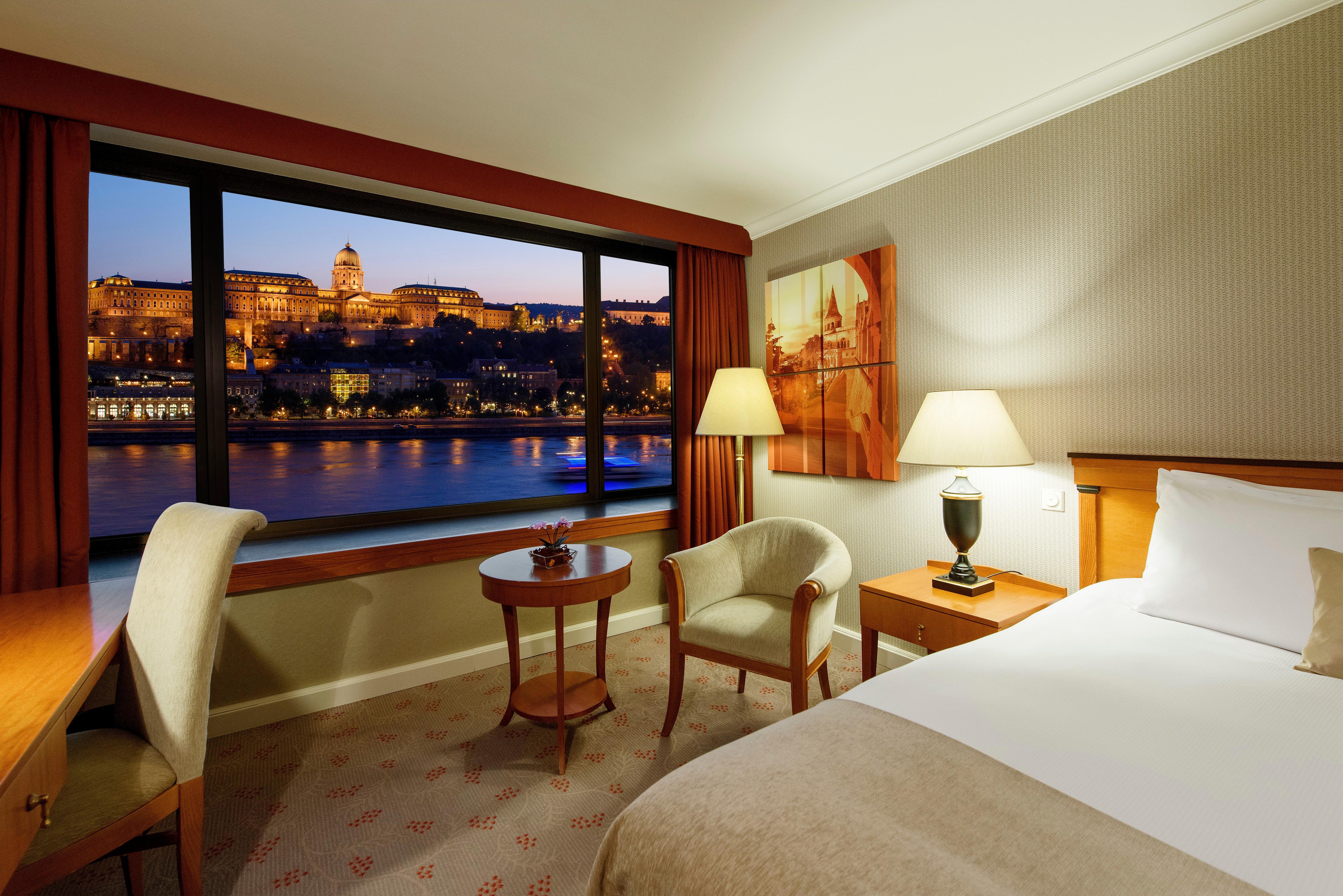 Intercontinental Budapest By Ihg Esterno foto The photo shows a hotel room featuring a cozy and well-lit interior. There is a comfortable bed with neutral-colored bedding positioned against one wall. To one side, there's a small wooden table with two chairs, creating a relaxing seating area. A s