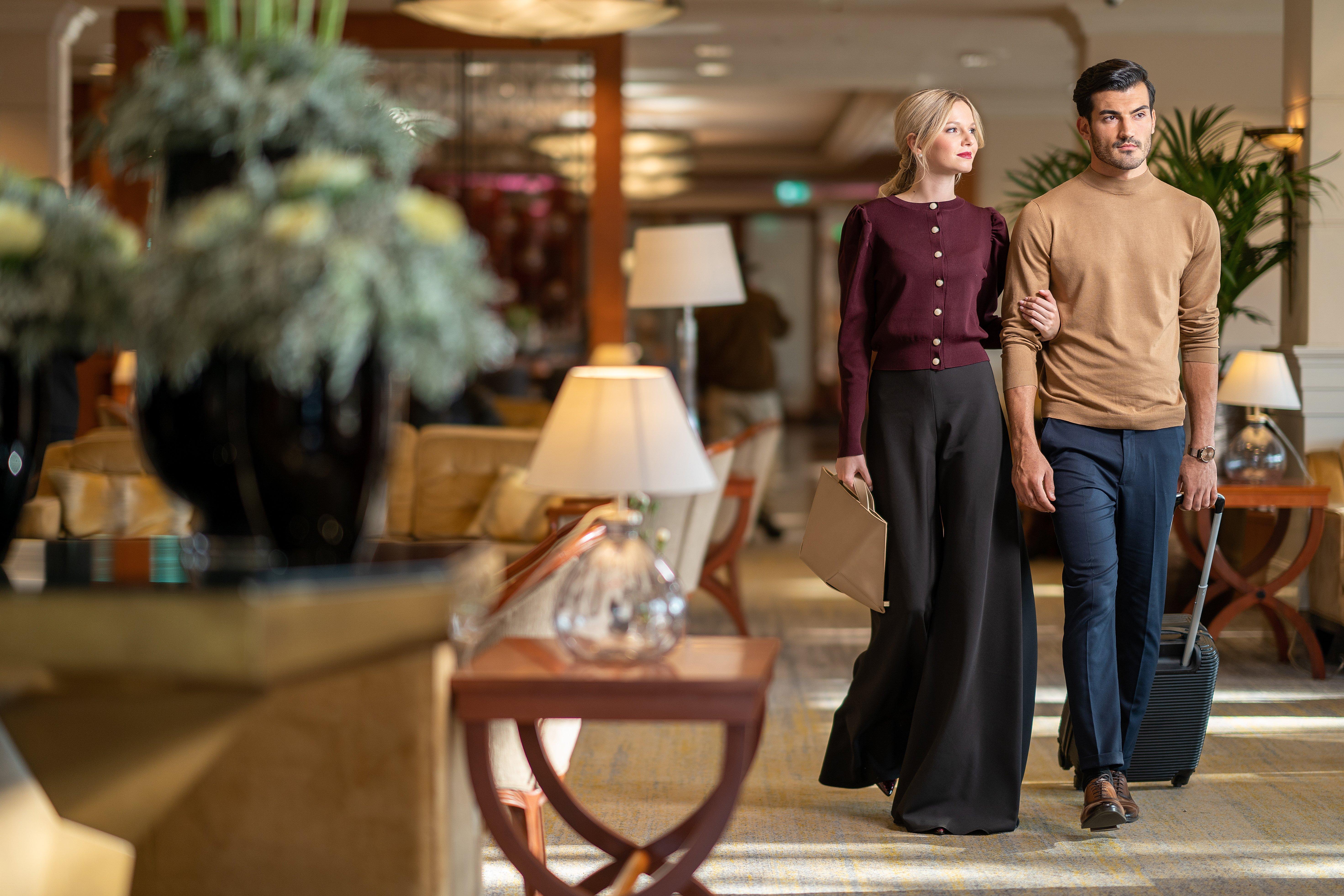 Intercontinental Budapest By Ihg Esterno foto The photo shows a stylish couple walking together in an elegant indoor setting, likely in a hotel or upscale venue. The woman is wearing a burgundy cardigan and wide-legged black trousers, while the man is dressed in a light brown sweater and dark je