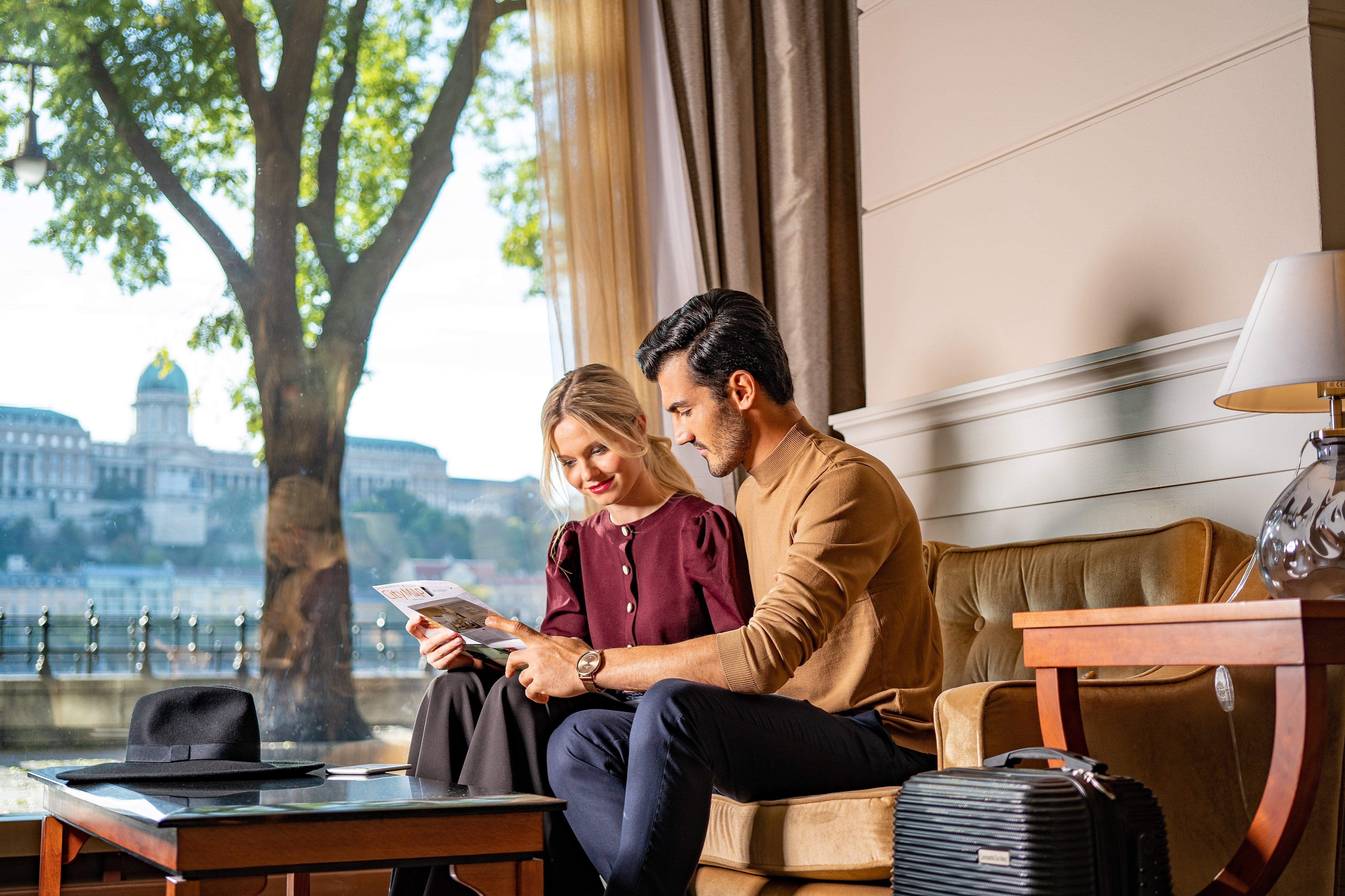 Intercontinental Budapest By Ihg Esterno foto The photo shows a couple sitting together on a couch in a well-lit room. They are looking at something on a piece of paper or a document. The man, dressed in a tan sweater, is focused intently on the paper, while the woman beside him, wearing a dark 