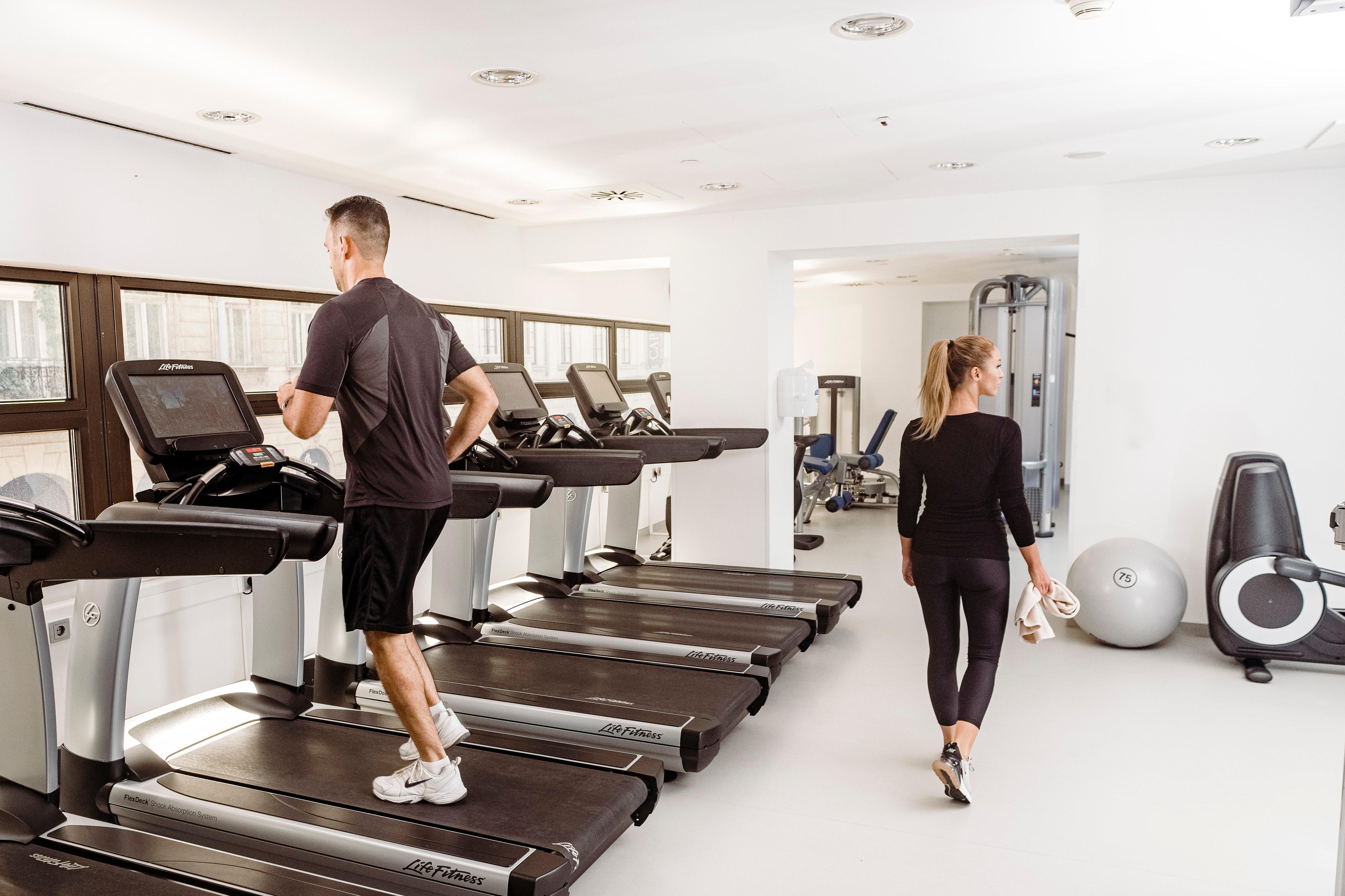Intercontinental Budapest By Ihg Esterno foto The photo shows a bright, modern gym. In the foreground, a man is running on a treadmill. He is dressed in athletic wear, consisting of a short-sleeve shirt and shorts. In the background, a woman is walking past him, also in athletic clothing. The gy