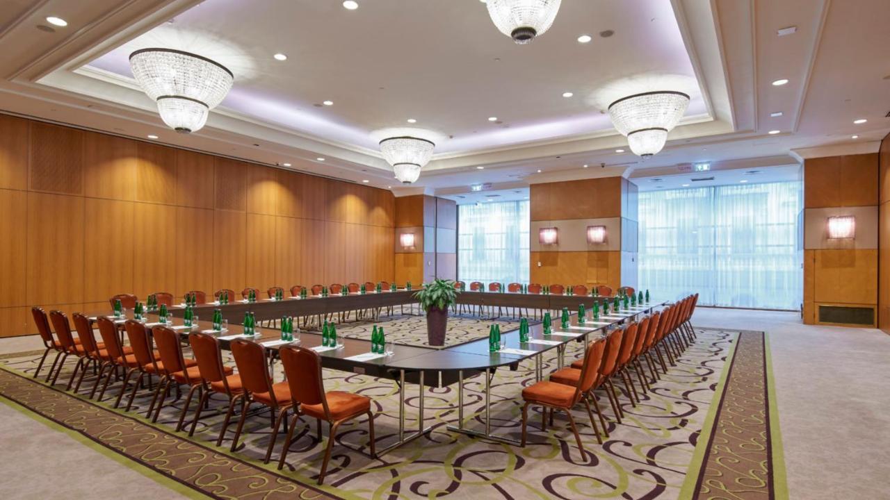Intercontinental Budapest By Ihg Esterno foto The photo shows a well-organized conference room set up for a meeting or seminar. It features a large rectangular table at the center, surrounded by numerous chairs arranged in a circular or U-shape configuration. The chairs are upholstered in a warm
