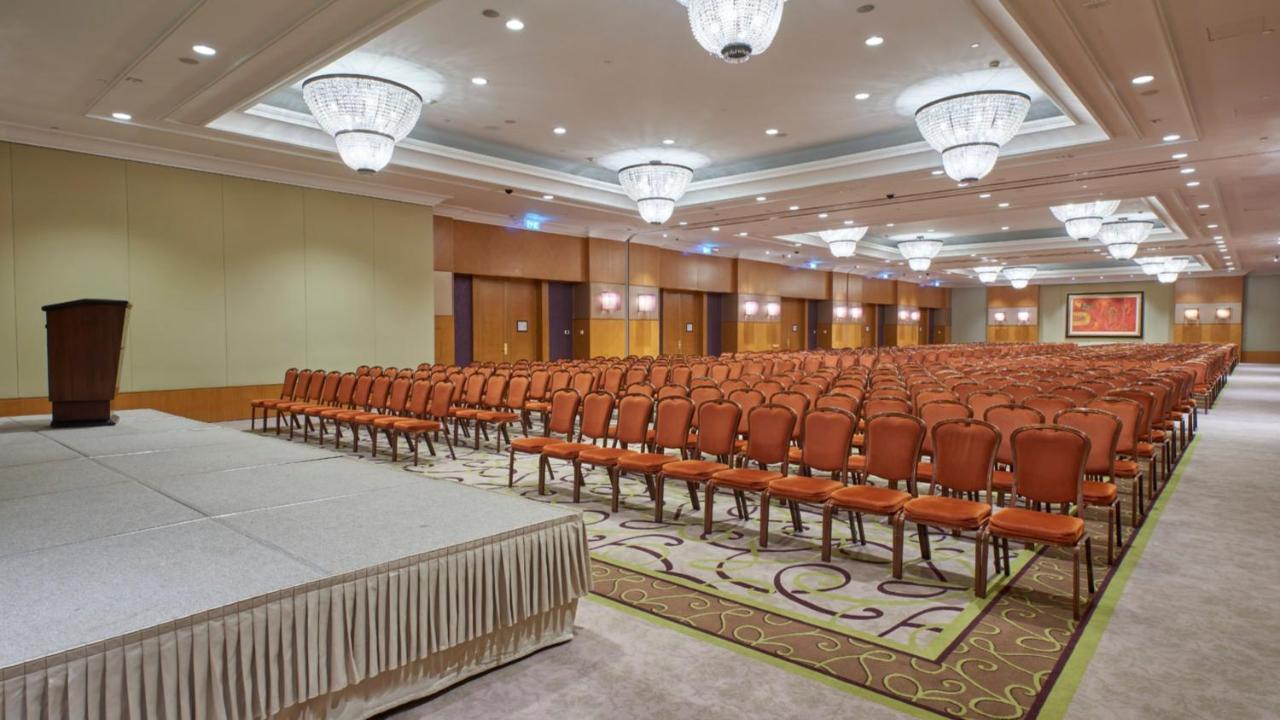 Intercontinental Budapest By Ihg Esterno foto The photo shows a spacious conference room or event hall. There is a large area filled with rows of orange chairs arranged in a neat, organized manner, indicating it is set up for a presentation or meeting. At the front, there is a raised platform wi