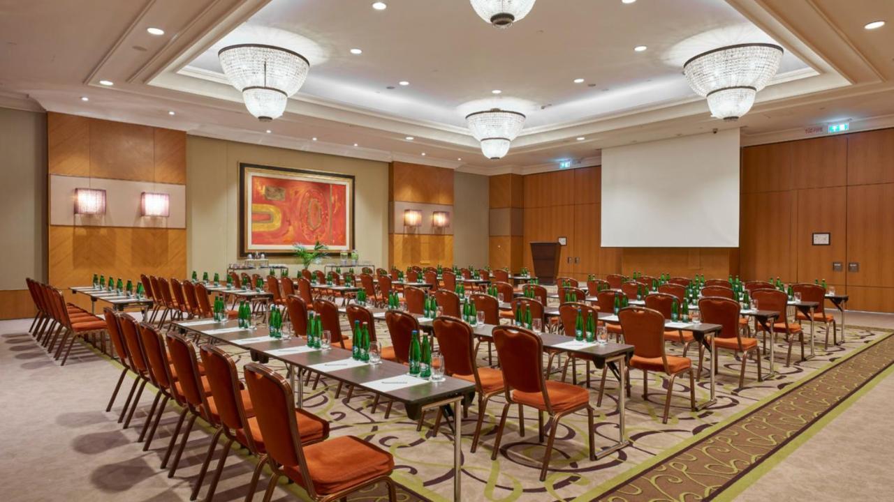 Intercontinental Budapest By Ihg Esterno foto The photo shows a spacious conference room set up for an event. There are multiple rows of chairs arranged in a classroom style, with each chair paired with a small table. The chairs are primarily upholstered in a reddish-brown color. There are also 