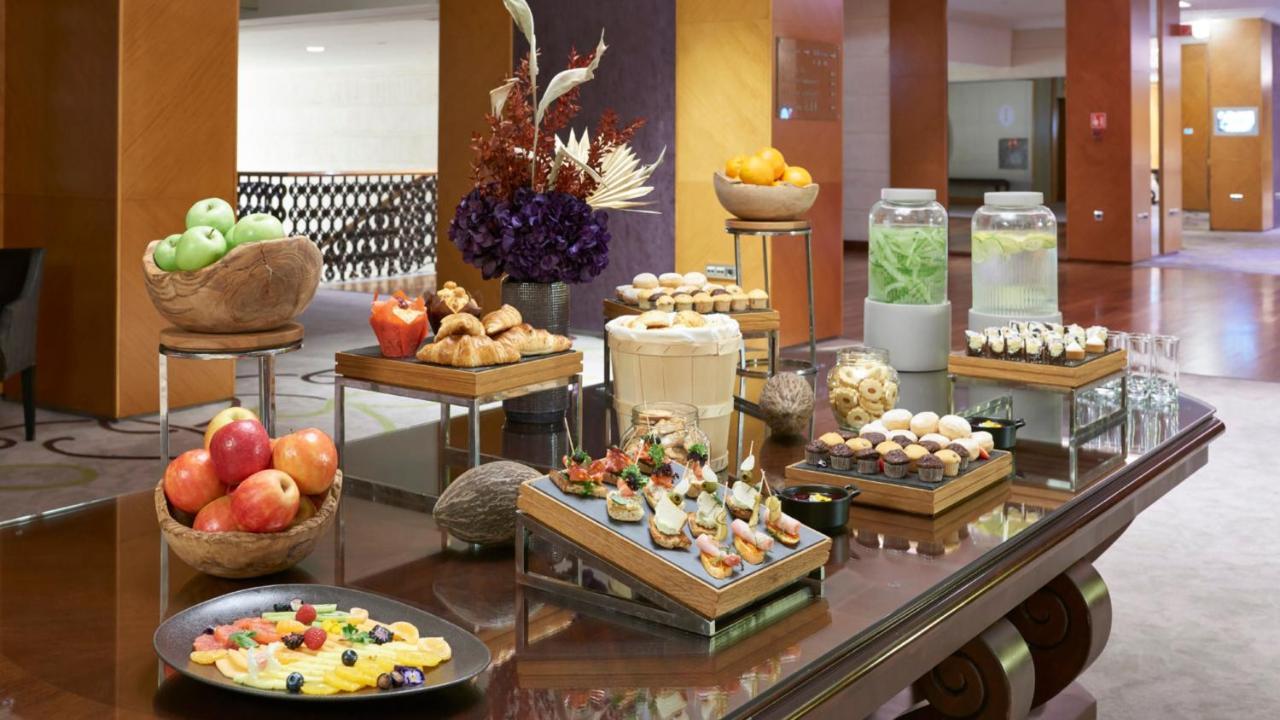 Intercontinental Budapest By Ihg Esterno foto The photo showcases an elegant display of a variety of foods, likely set up in a buffet or catering arrangement. There are multiple wooden trays and platters featuring an assortment of items:

1. **Fruits**: There are green and red apples, along with
