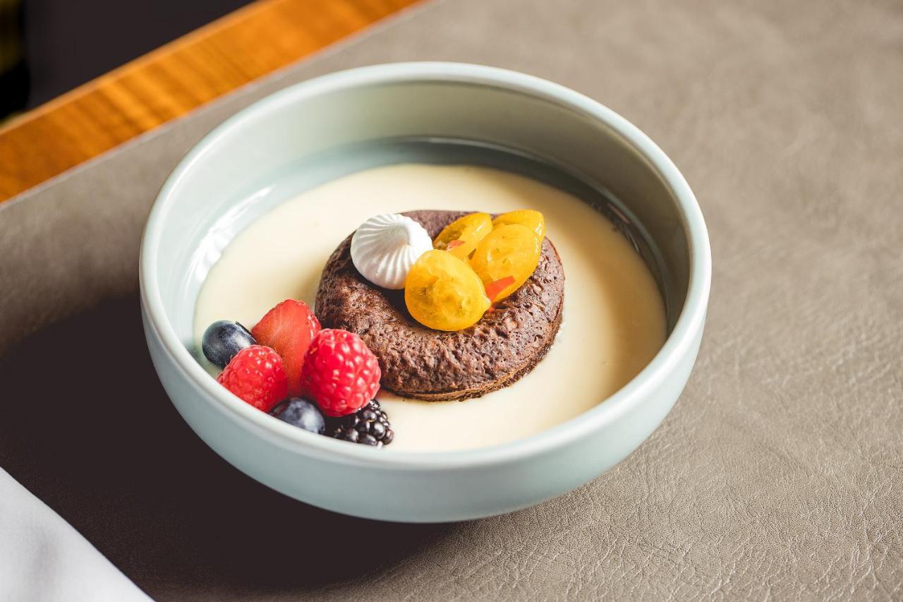 Intercontinental Budapest By Ihg Esterno foto The photo shows a dessert presented in a light blue bowl. At the center, there is a round chocolate cake or cookie topped with small pieces of yellow fruit, possibly apricots or peaches. Surrounding the cake are various fresh berries, including raspb
